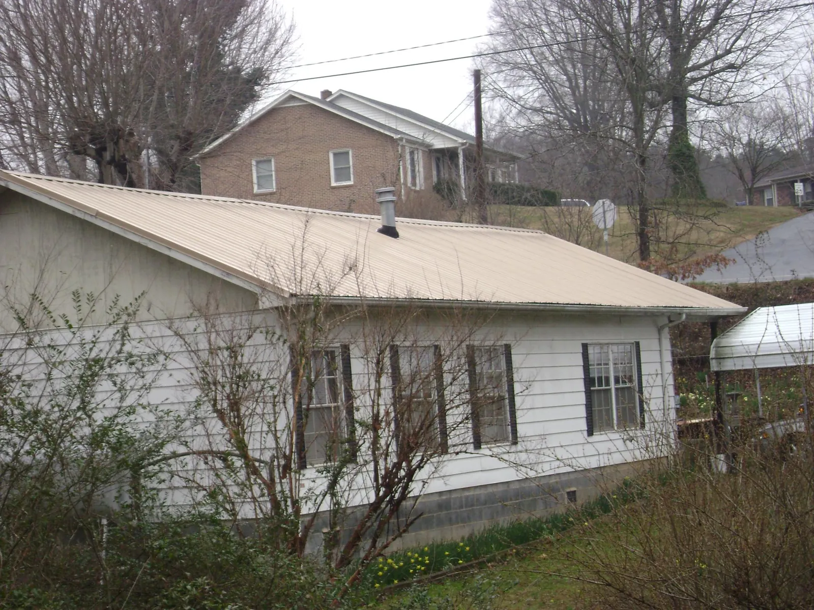 Tan metal roof on a white sided house set into a hillside — Commercial Roofing by Roofing Brothers in Hampton